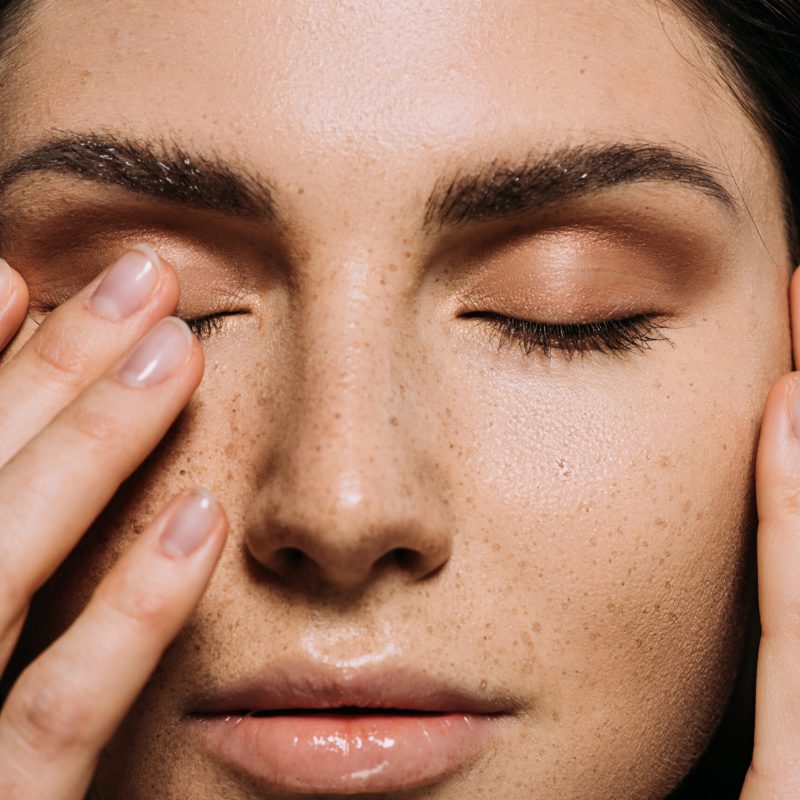 close up view of tender girl with freckles on face touching closed eyes