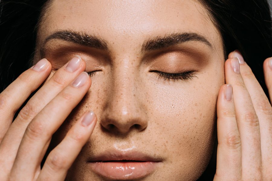 close up view of tender girl with freckles on face touching closed eyes