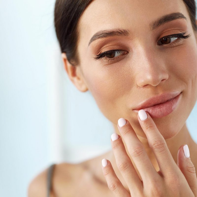 Lips Skin Care. Beautiful Woman With Beauty Face Applying Lip Balsam, Lipbalm On Full Sexy Lips. Portrait Of Smiling Female Model With Soft Skin And Natural Nude Makeup Touching Lips. High Resolution