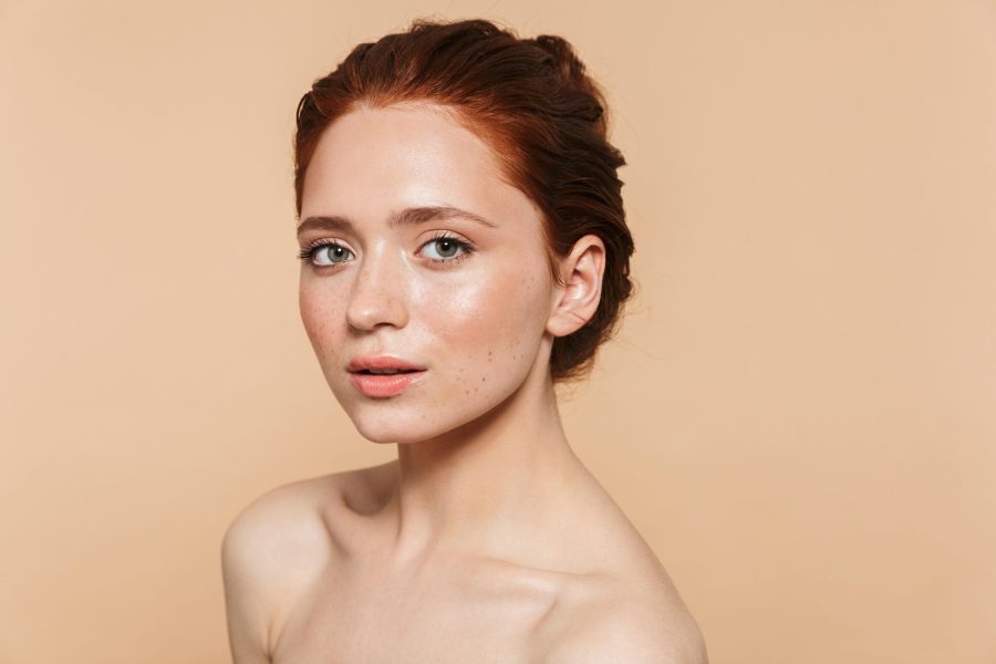 Image of a pretty young redhead woman posing isolated over beige wall background.