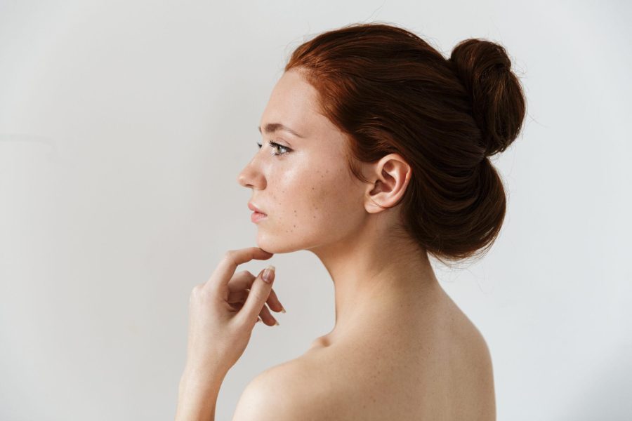 Beauty side view portrait of an attractive sensual young topless redhead woman standing isolated over gray background, posing