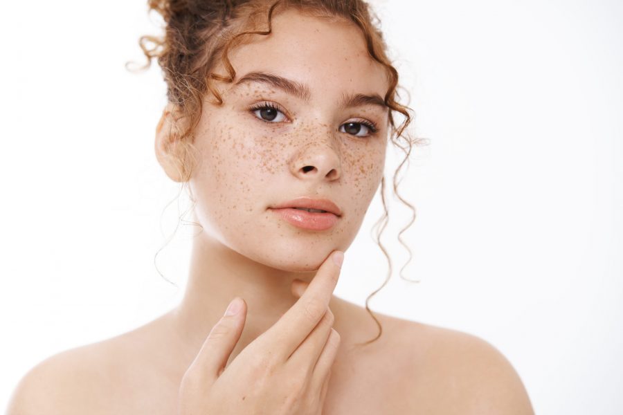 Attractive sensual gentle young redhead woman naked freckles cheeks accepting own body-positive touch skin applying skincare product, go shower, standing white background bathroom. Copy space