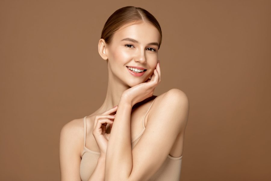 Skin care model. Beautiful young woman with perfect skin touching her face and posing against beige background. Beauty treatment and spa concept.