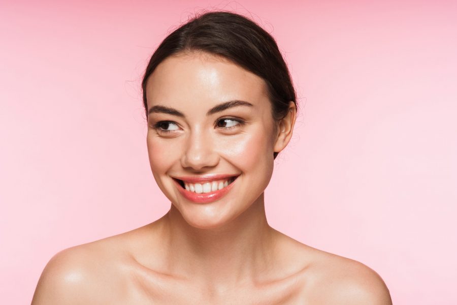 Beauty portrait of a beautiful smiling young topless brunette woman standing isolated over pink background