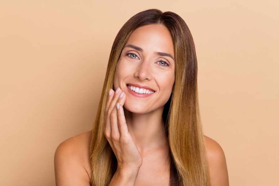 Portrait of attractive cheery long-haired woman touching soft flawless skin lifting uplift isolated over beige pastel color background.